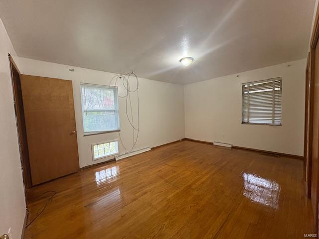 unfurnished room with baseboards, wood finished floors, and baseboard heating