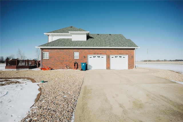 view of property exterior with a wooden deck, a shingled roof, an attached garage, and brick siding