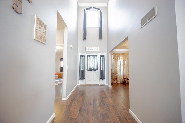 foyer entrance with baseboards, visible vents, wood finished floors, and a towering ceiling