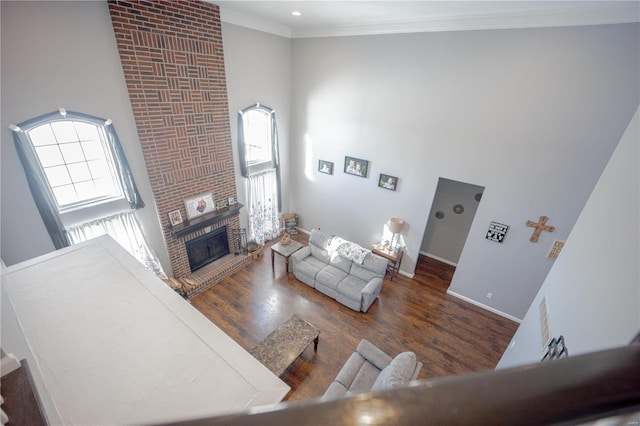 living room with wood finished floors, ornamental molding, a fireplace, baseboards, and a towering ceiling