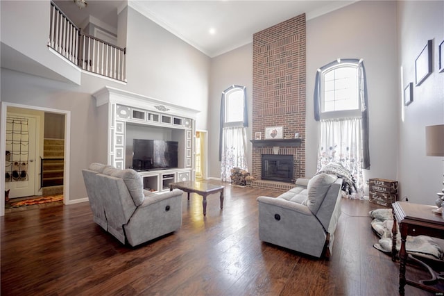 living room with a brick fireplace, a towering ceiling, wood finished floors, and plenty of natural light