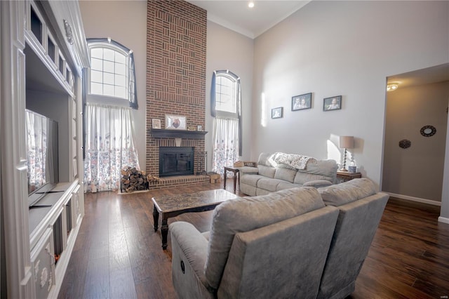living room featuring crown molding, baseboards, dark wood-style flooring, a fireplace, and a towering ceiling