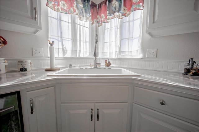 kitchen with beverage cooler, light countertops, white cabinets, a textured wall, and a sink