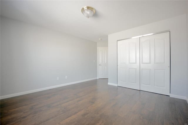 unfurnished bedroom featuring a closet, dark wood finished floors, and baseboards