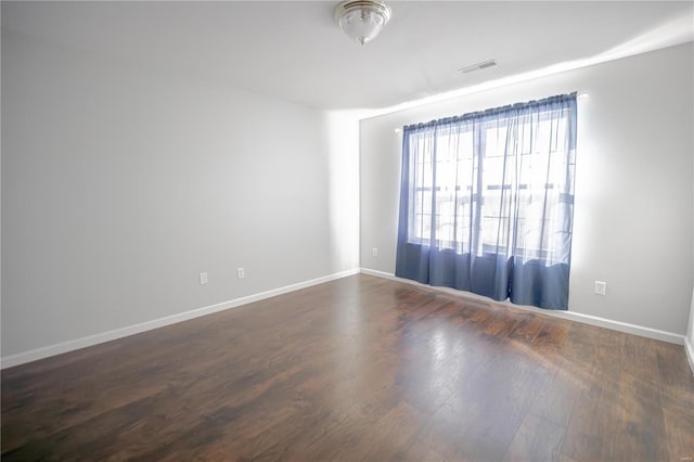 empty room featuring visible vents, baseboards, and dark wood finished floors