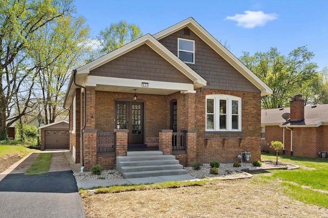 view of front facade with a detached garage, covered porch, brick siding, an outdoor structure, and aphalt driveway