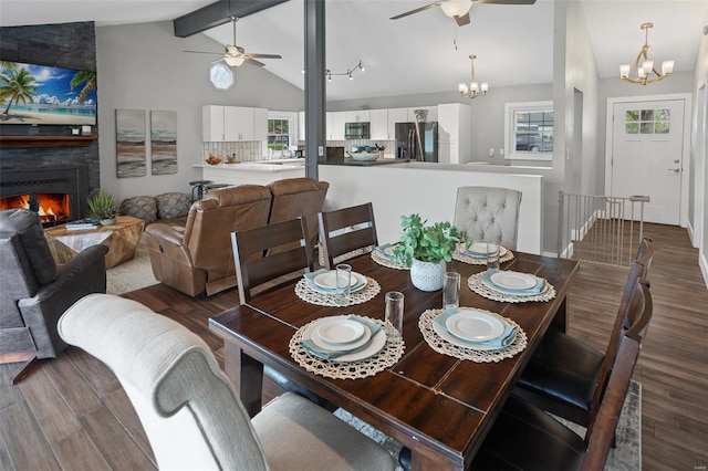 dining room featuring wood finished floors, vaulted ceiling with beams, a large fireplace, and ceiling fan with notable chandelier