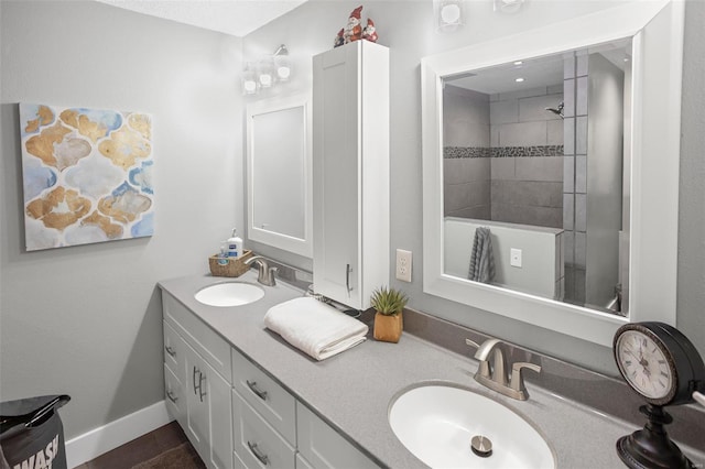 bathroom featuring a tile shower, baseboards, a sink, and double vanity