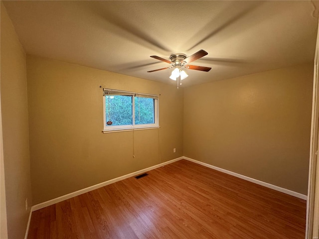 unfurnished room with baseboards, wood finished floors, visible vents, and a ceiling fan