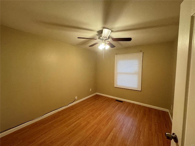 empty room with wood finished floors, visible vents, a ceiling fan, and baseboards