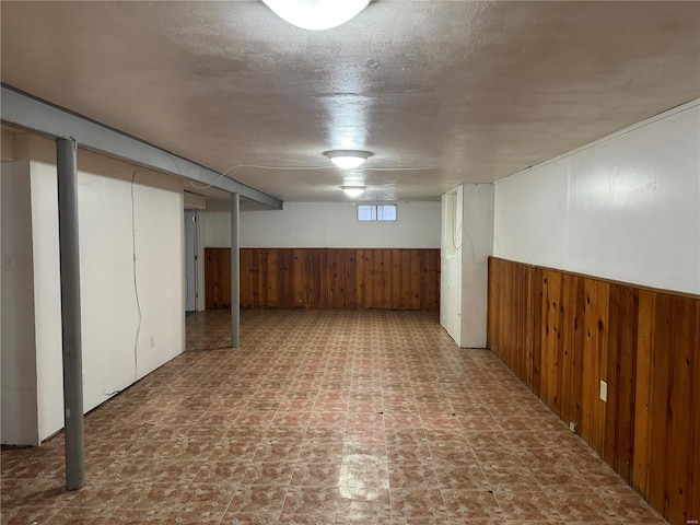 basement featuring wooden walls, a textured ceiling, and a wainscoted wall