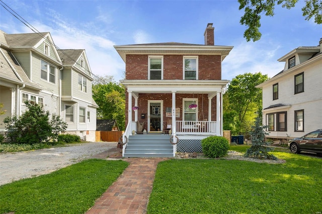 traditional style home with brick siding, a front lawn, a chimney, and a porch