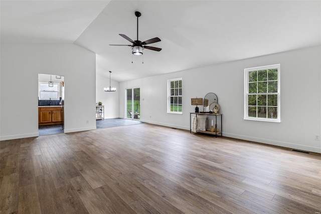 unfurnished living room with plenty of natural light, dark wood finished floors, visible vents, and ceiling fan with notable chandelier