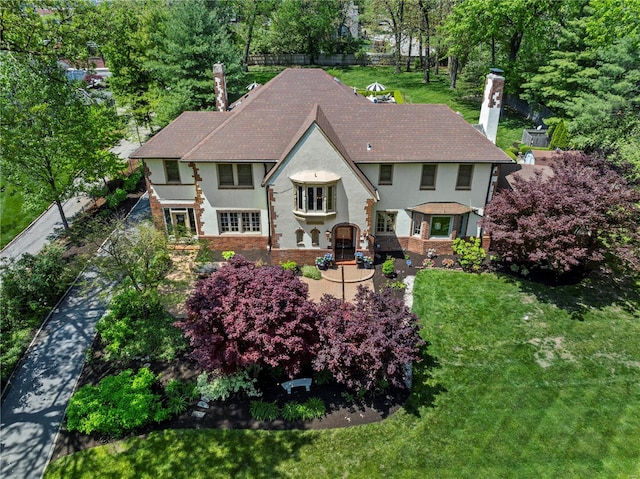 back of property featuring a lawn, stucco siding, a chimney, and roof with shingles
