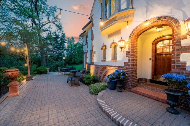 exterior entry at dusk featuring brick siding, outdoor dining space, and a patio area