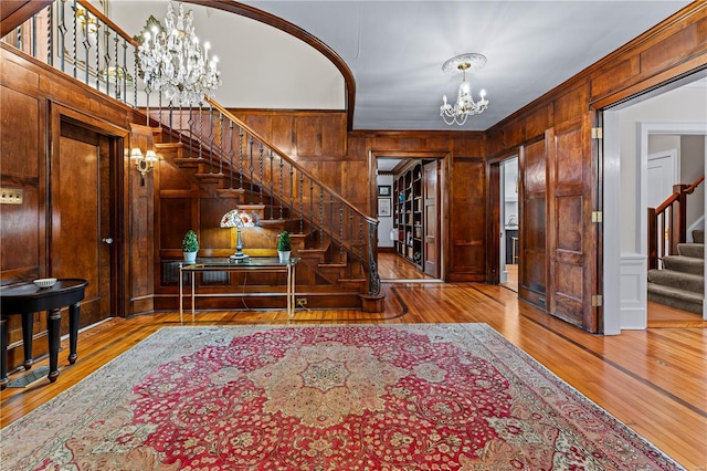 foyer entrance featuring ornamental molding, stairs, hardwood / wood-style floors, wooden walls, and a notable chandelier