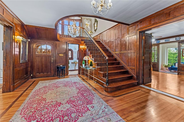 foyer entrance featuring wooden walls, stairway, light wood-type flooring, and a chandelier