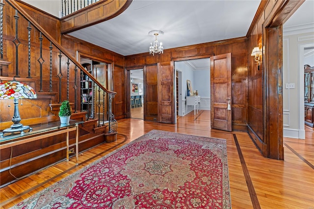 foyer entrance with wood walls, a chandelier, ornamental molding, and stairway