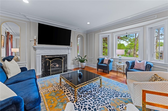 living room with crown molding, a high end fireplace, wood finished floors, a decorative wall, and recessed lighting