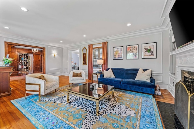 living area featuring crown molding, a decorative wall, recessed lighting, hardwood / wood-style floors, and a premium fireplace