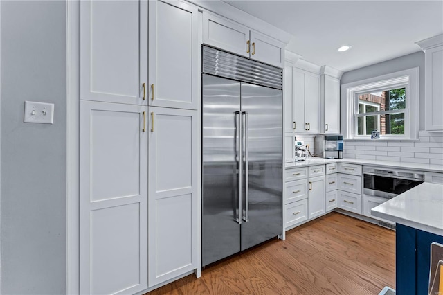 kitchen featuring light wood-style floors, white cabinetry, built in fridge, tasteful backsplash, and light stone counters