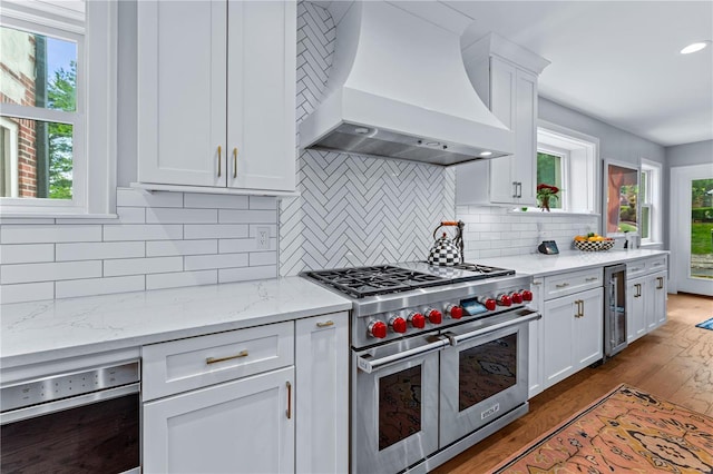kitchen featuring beverage cooler, light wood-style flooring, white cabinetry, double oven range, and custom exhaust hood