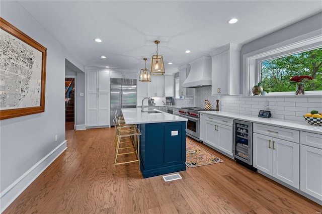 kitchen with decorative backsplash, high quality appliances, visible vents, premium range hood, and wine cooler
