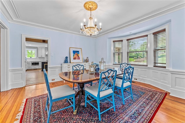 dining room featuring crown molding, a wainscoted wall, an inviting chandelier, a decorative wall, and light wood-style flooring