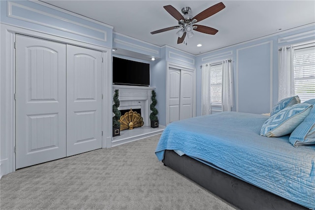 carpeted bedroom featuring multiple closets, multiple windows, a fireplace with raised hearth, and a ceiling fan