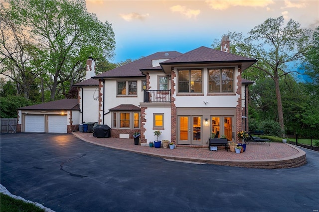view of front of home featuring french doors, a chimney, a detached garage, a balcony, and stucco siding