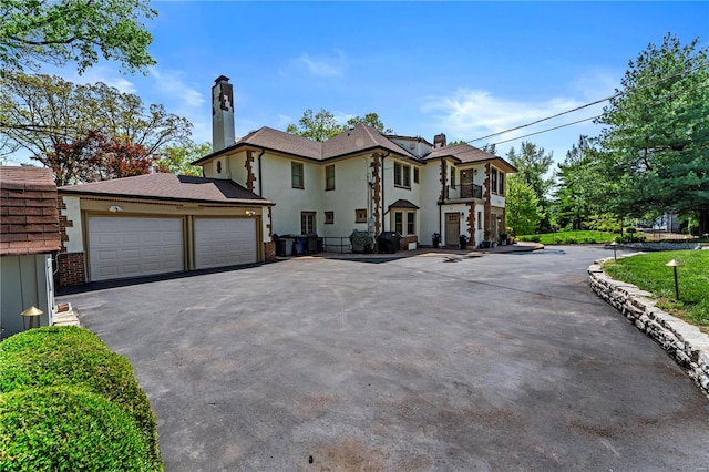 view of front of home with a garage, a chimney, driveway, and a balcony