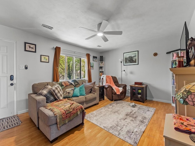 living area featuring a ceiling fan, light wood-style floors, a fireplace, baseboards, and visible vents