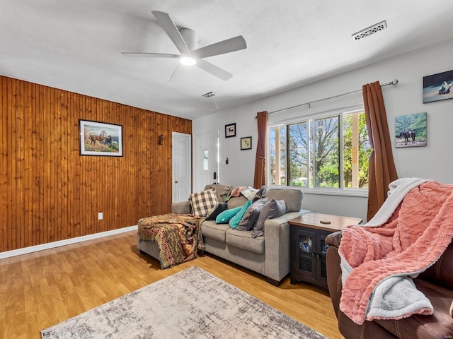 living room featuring wooden walls, wood finished floors, visible vents, and ceiling fan
