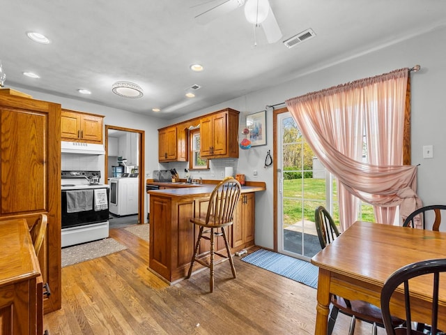 kitchen with electric stove, light wood-style flooring, a peninsula, under cabinet range hood, and visible vents