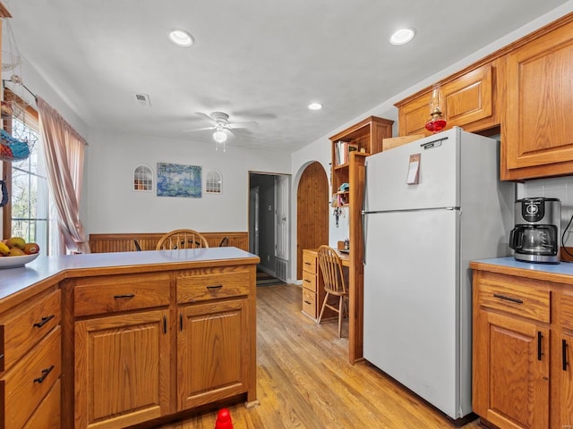 kitchen featuring brown cabinetry, wainscoting, light wood-type flooring, visible vents, and freestanding refrigerator