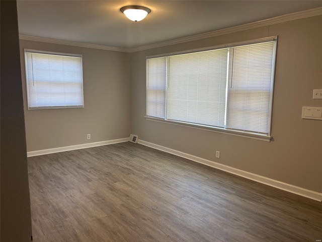 empty room featuring a wealth of natural light, dark wood finished floors, baseboards, ornamental molding, and visible vents