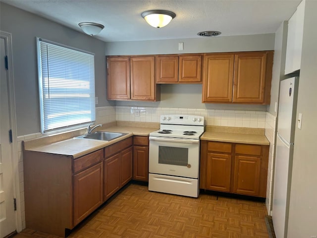 kitchen featuring brown cabinets, light countertops, a sink, and white appliances