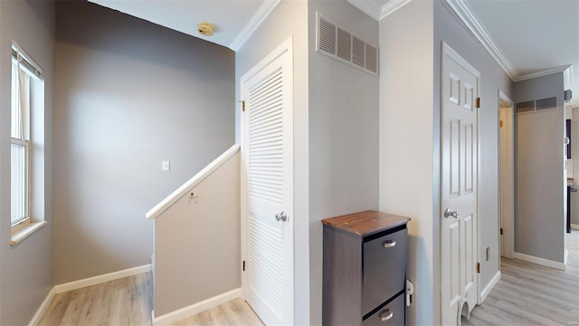 hall with light wood finished floors, baseboards, visible vents, and crown molding