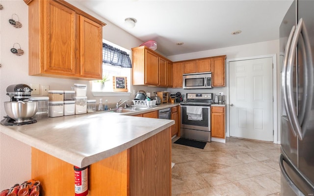 kitchen featuring a peninsula, brown cabinets, a sink, light countertops, and appliances with stainless steel finishes