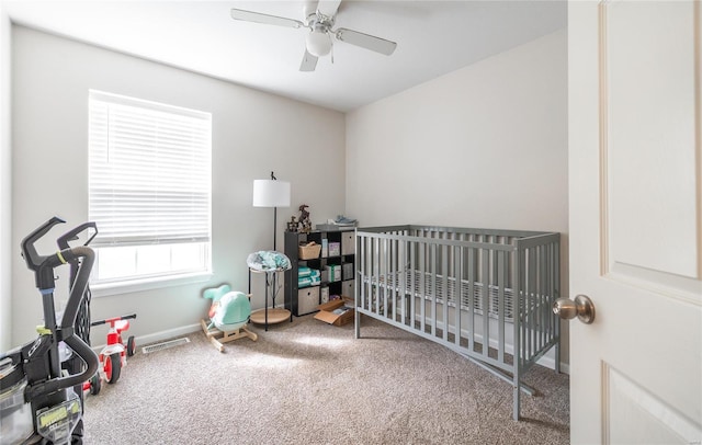 bedroom with carpet, a nursery area, visible vents, baseboards, and ceiling fan