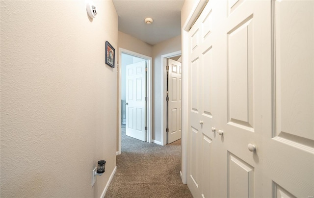 hallway featuring baseboards and dark carpet