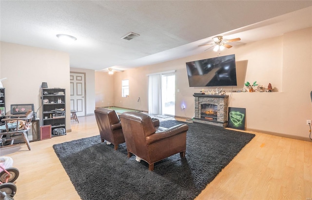 living room featuring visible vents, wood finished floors, a ceiling fan, and a stone fireplace