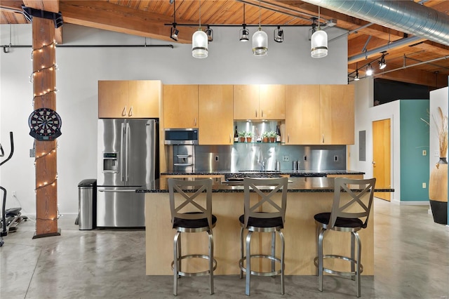 kitchen featuring a kitchen breakfast bar, concrete floors, a center island, stainless steel appliances, and a towering ceiling