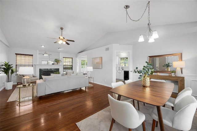 dining space with vaulted ceiling, visible vents, ceiling fan with notable chandelier, wood finished floors, and a high end fireplace