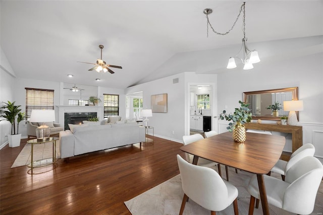 dining area with wood finished floors, ceiling fan with notable chandelier, a fireplace, lofted ceiling, and visible vents