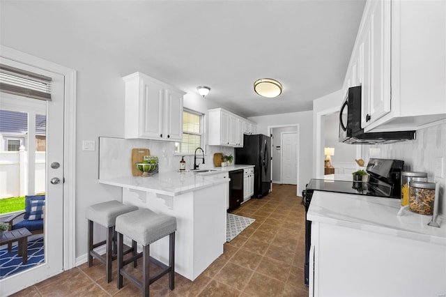 kitchen with white cabinets, a kitchen breakfast bar, a sink, backsplash, and black appliances