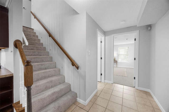 interior space featuring stairway, light tile patterned floors, baseboards, a textured ceiling, and light colored carpet