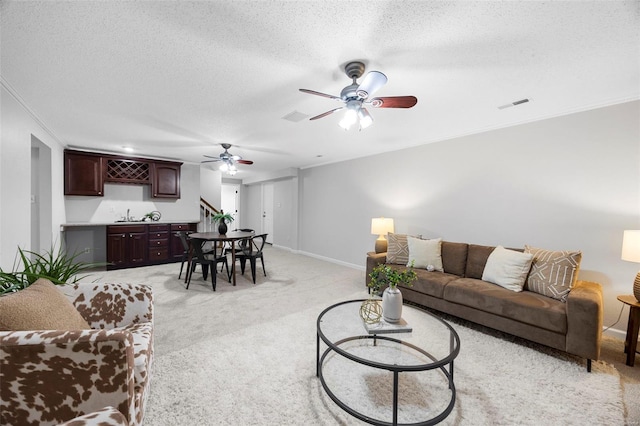 living area with crown molding, a textured ceiling, light carpet, wet bar, and visible vents