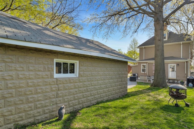 view of property exterior with central AC unit, an outdoor fire pit, an outdoor structure, a yard, and roof with shingles