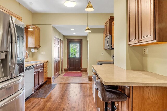 kitchen with decorative light fixtures, stainless steel appliances, light wood finished floors, and a sink
